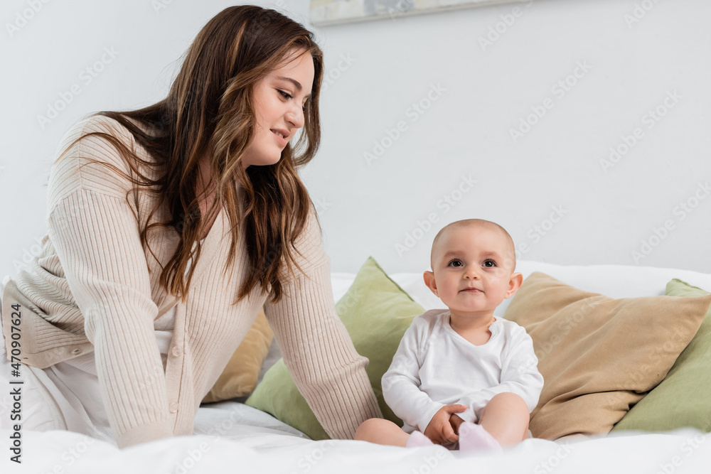 Smiling mother with overweight looking at baby girl on bed. Smiling mother with overweight looking at baby girl on bed.