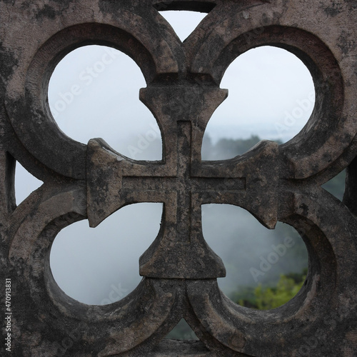 Aesthetics of fairytale details: square part of the old stone fence of the castle balcony: the window with the image of the cross. Pena Palace, mountain fog in Sintra, Portugal