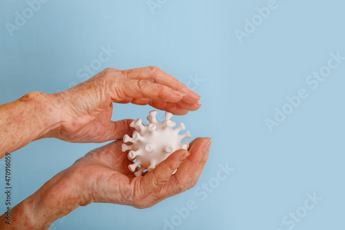 A hands of a senior woman are holding a model of coronovirus on blue background. Coronovirus molecule printed model on a 3D printer.