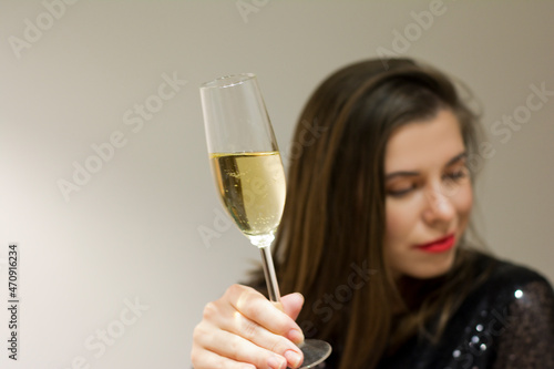 Selective focus of champagne glass in hands of elegant woman with covered eyes isolated on gray blurred background. Concept: celebrate new year Valentine's Day Women's Day birthday holiday party 