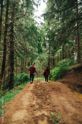 Man and woman hikers in red shirts walking on a mountain road in a coniferous forest, view from the back. Vertical © bodnarphoto