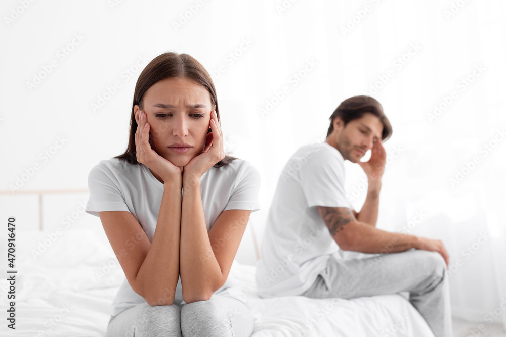 Sad unhappy upset resentful european young wife ignores husband after quarrel, sitting in bed Sad unhappy upset resentful european young wife ignores husband after quarrel, sitting in bed