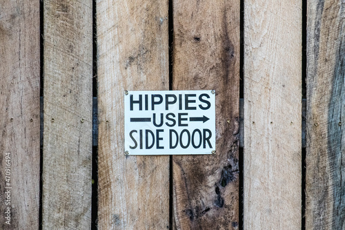An old vintage funny humorous sign says hippies use side door showing the bias and prejudice in the culture in the 1960s and 1970s.