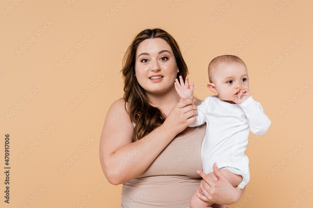Smiling plus size parent holding hand of baby daughter isolated on beige. Smiling plus size parent holding hand of baby daughter isolated on beige.
