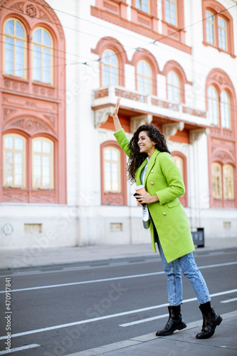 Young woman holding takeaway coffee and calling a taxi on the street