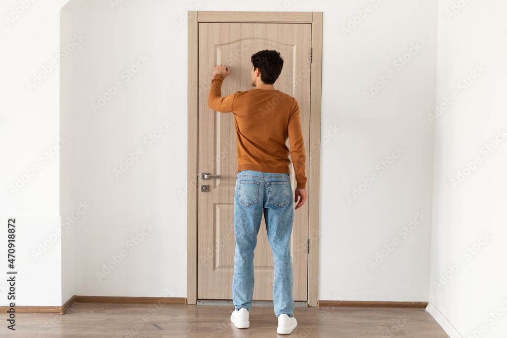 Rear back view of man knocking on the wooden door - obrazy, fototapety, plakaty 