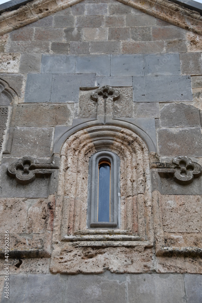 A narrow small window in the wall of an old stone house. Carved stone window.