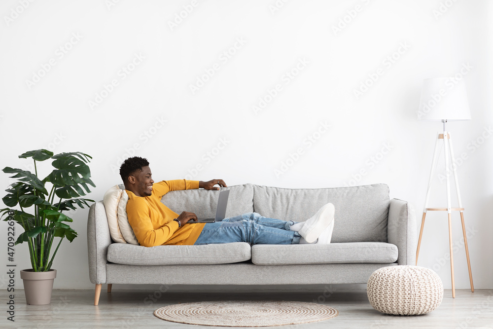 Carefree african american man reclining on sofa with notebook