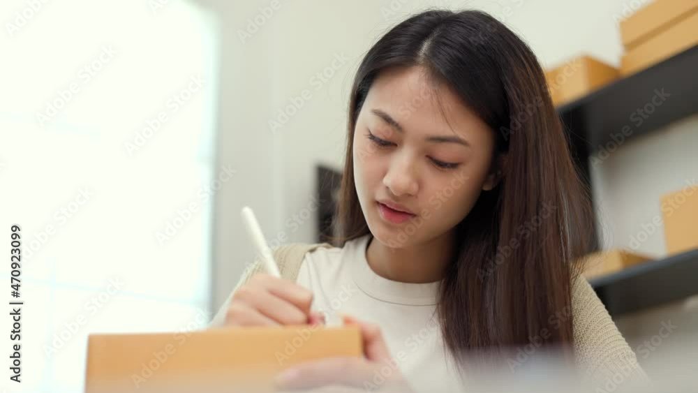 Young asian business woman writing address to sending product to customer. Online business working at home. Startup Small business owner entrepreneur Young asian business woman writing address to sending product to customer. Online business working at home. Startup Small business owner entrepreneur