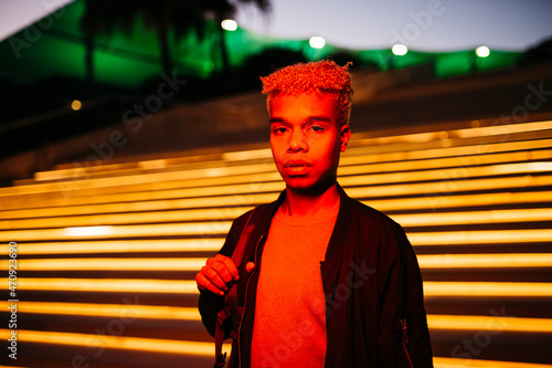 Young latin american student male under a red light walking on the street at dusk photo