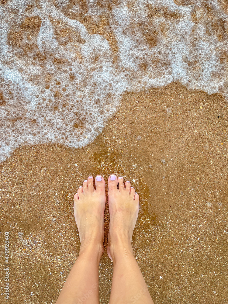 Top view of bare feet in the sand on the beach. Copy space - Foamy sea texture on the background of the sea, standing barefoot on the beach