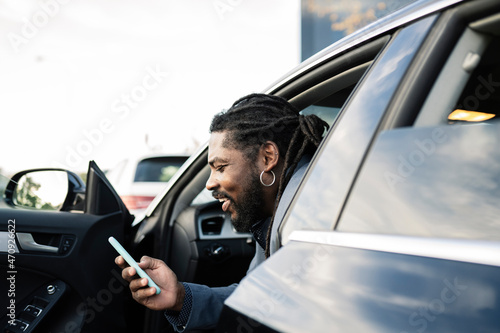 Attractive afro man gets out of the car smiling while using his phone