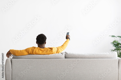 Quadro em tela Back view of black man sitting on couch with remote