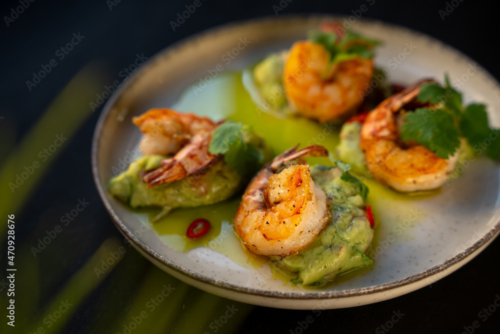 Appetizer with shrimps served with guacamole and greens on white plate on black background. Delicious, beautiful, healthy snack. Modern cuisine Appetizer with shrimps served with guacamole and greens on white plate on black background. Delicious, beautiful, healthy snack. Modern cuisine