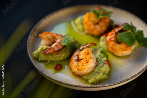 Appetizer with shrimps served with guacamole and greens on white plate on black background. Delicious, beautiful, healthy snack. Modern cuisine