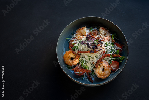 Appetizer with shrimps. Salad with greens, vegetables and cheese on black background. Delicious, beautiful, healthy snack. Modern cuisine. Top view