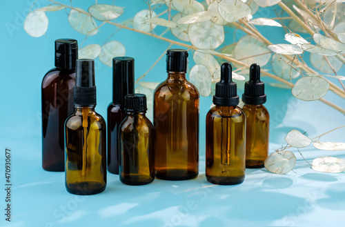 Brown glass bottles of cosmetic products on a blue background. Natural cosmetics concept. Cosmetic products decorated with dried flowers. Natural organic spa beauty cosmetic concept. Container for oil