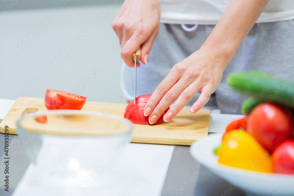 Close up of a girl hands slicing tomato with a knife on a cutting board for a vegan vitamin vegetable salad and putting them in a glass bowl while cooking breakfast in the kitchen