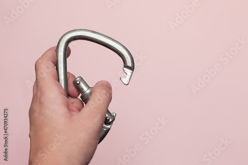 Carabiner for work at height. Climbing equipment on a pink background, carabiner in hand