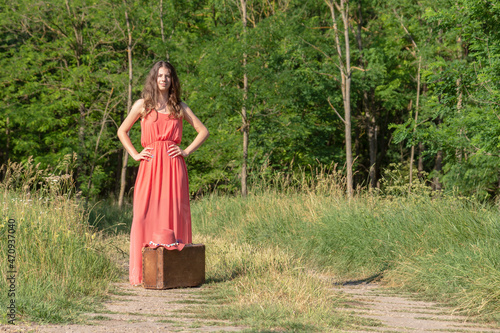 Woman standing in forest road with old suitcase