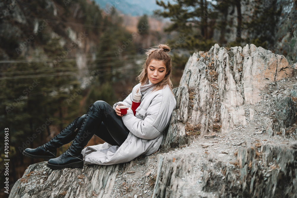 Fototapeta premium Travel girl drinking hot tea from thermos on forest and mountain background. Girl on vacation enjoying the beauty of nature. Camping hiking lifestyle. Altai mountains