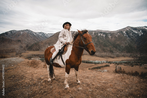 Beautiful young female horse owner taking care of her horse with mountain on background. Animal and people frienship concept. Autumn in Altai