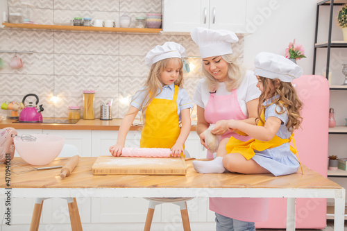 Happy caucasian mother helping her preschool daughters rolling dough