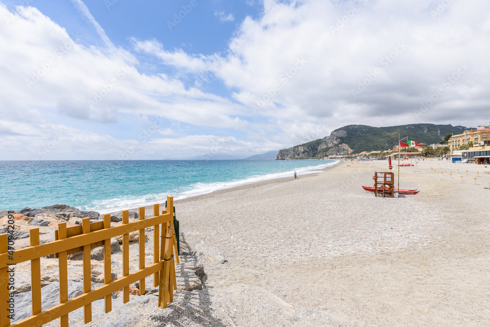 Finale Ligure. May 21, 2021. View from the Pier of Finalpia on an empty stretch of beach with a wooden lifeguard spot and a small rescue boat and few people strolling.