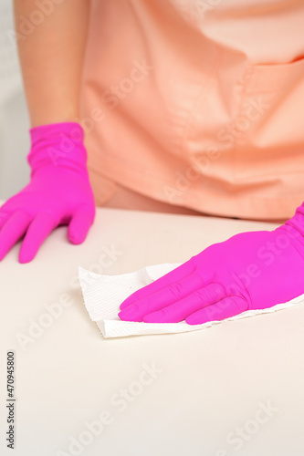 Close up of hands in rubber protective pink gloves cleaning the white surface with a white rag