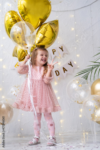 Photography happy little blond girl in pink dress holding balloons and celebrating her birth