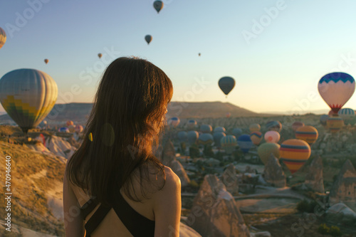 Young woman watching the sunrise and hot air balloons taking off over valley in Cappadocia, Goreme, Turkey photo