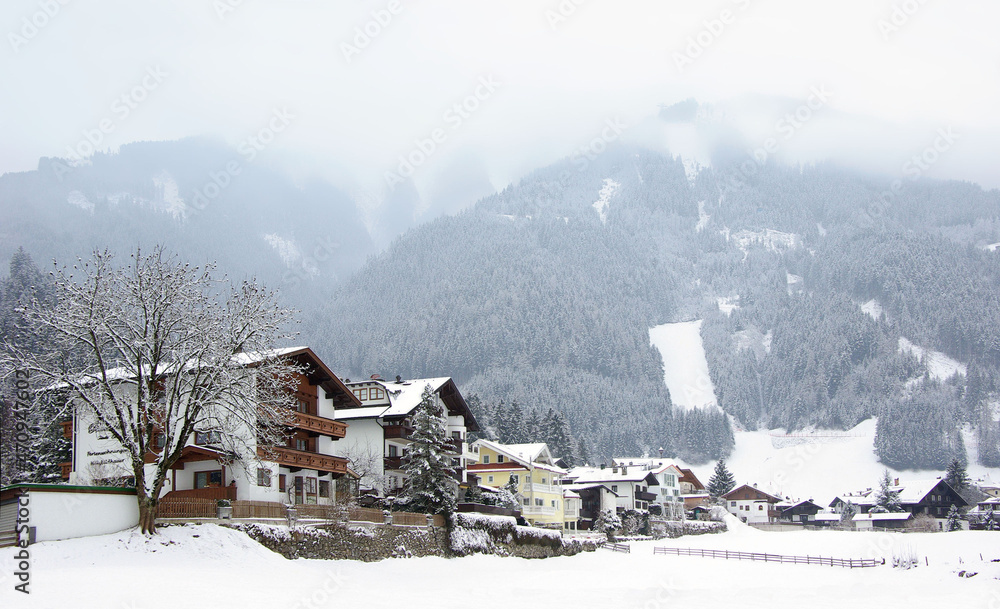 Winter view of residential buildings in Mayrhofen village and Ahorn mountain at background, covered with clouds