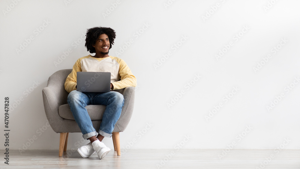Fototapeta premium Smiling Black Guy With Laptop Computer Sitting In Chair And Looking Aside