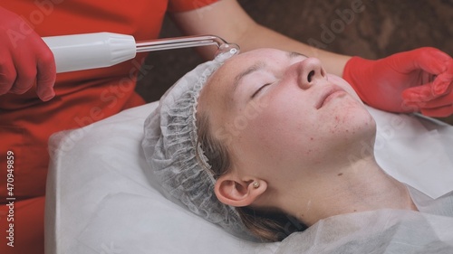 A beautician makes a darsonvalization of the face of a young girl with problem skin. photo