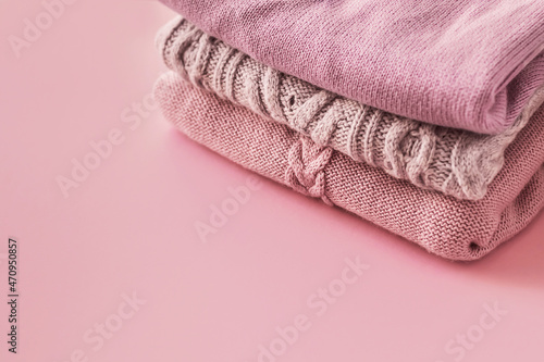 Stack of cozy winter autumn sweaters in pink pastel colors on a pink background. Knitted wool sweaters. Fashion and style. Copy space.