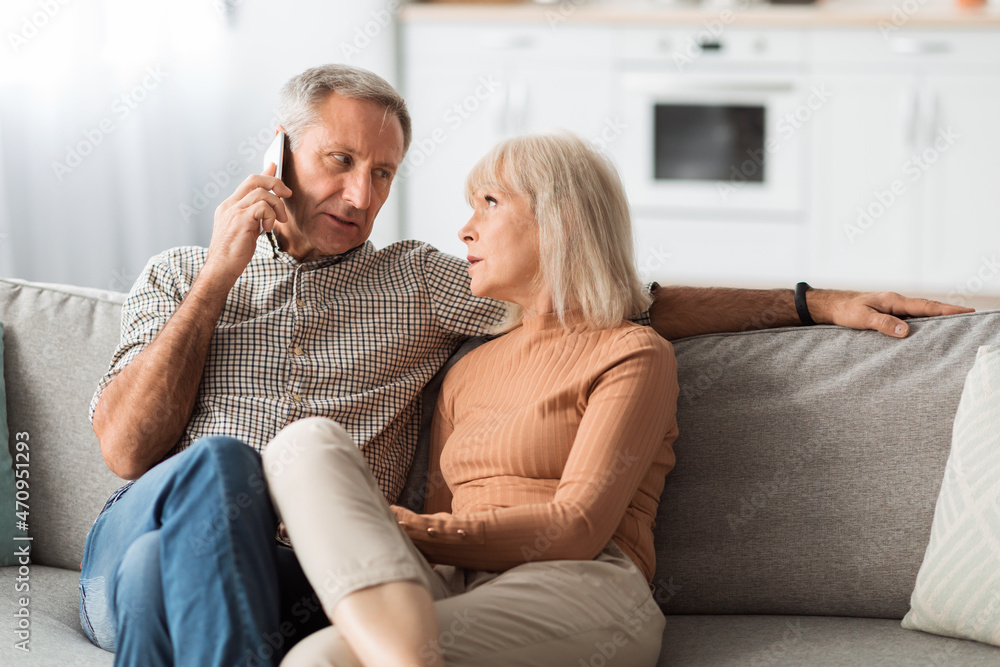 Senior Husband Talking On Phone Looking At Wife At Home Senior Husband Talking On Phone Looking At Wife At Home
