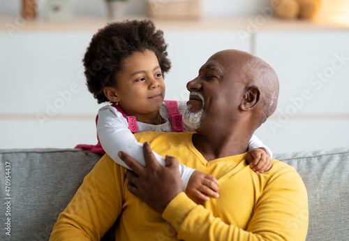 Фотография Cheerful little black girl play with older grandfather from back, hugging man at