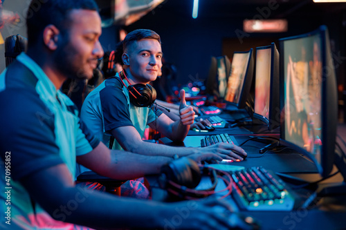 Caucasian young man happy with his game and showing thumbs-up gesture during participation in online esports competitions in gaming club