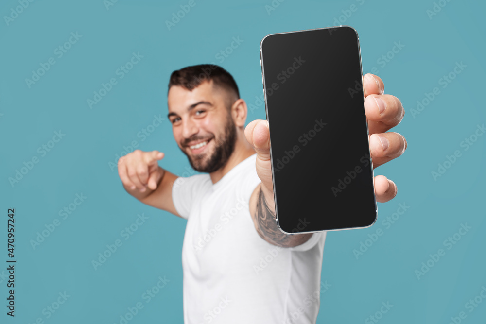 Smiling adult european guy show finger at phone with blank screen and recommends gadget Smiling adult european guy show finger at phone with blank screen and recommends gadget