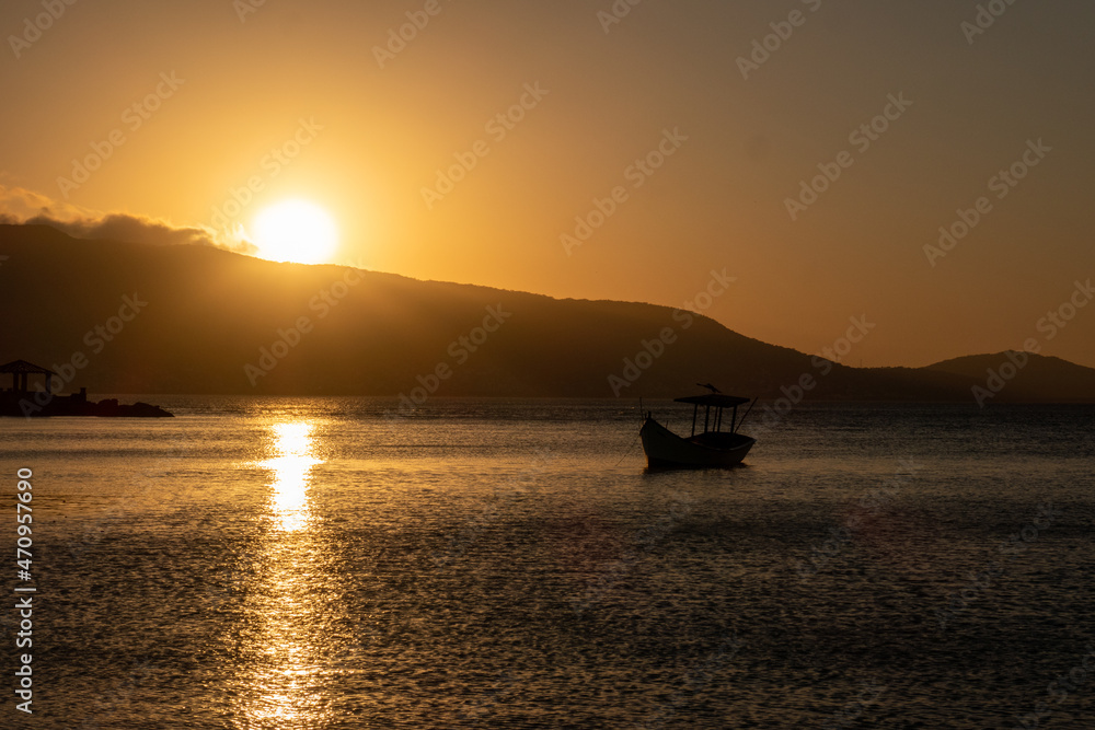 beautiful sunset overlooking the sea, in the background landscape with sun disappearing behind the mountains and yellow and orange sky