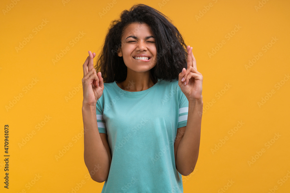 Studio portrait of cute dark skinned girl holding both hands with fingers crossed, isolated over bright colored yellow background Studio portrait of cute dark skinned girl holding both hands with fingers crossed, isolated over bright colored yellow background