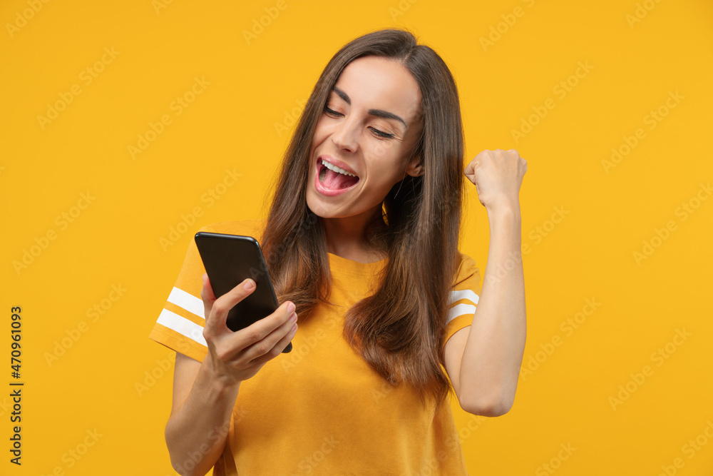 Portrait of euphoric soccer fan girl celebrating her favourite team victory and money win after betting at bookmaker's mobile application, making winner's gesture clenching her fist Portrait of euphoric soccer fan girl celebrating her favourite team victory and money win after betting at bookmaker's mobile application, making winner's gesture clenching her fist