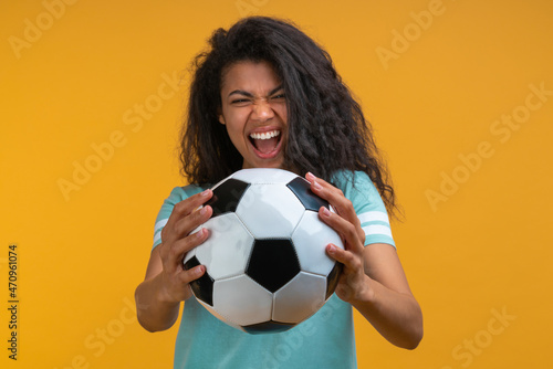 Studio image of soccer fan girl reaching the ball she's holding in hands to the camera with smiling and saying yeah face expression, being happy to support favorite team © wpadington