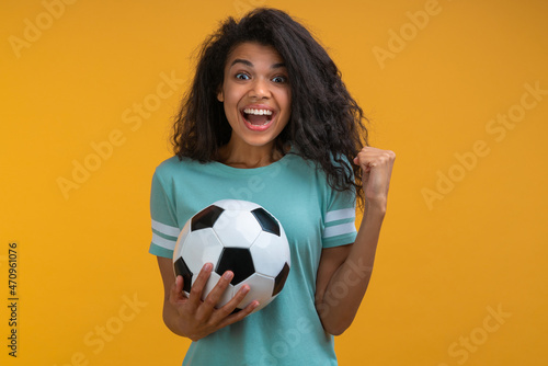 Excited happy soccer fan girl celebrating victory after betting at bookmaker's website, making winner's gesture clenching her fist while holding ball in hand © wpadington