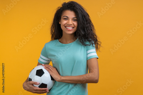 Portrait of attractive confident smiling soccer player girl posing with a ball in hands, isolated over bright colored yellow background © wpadington
