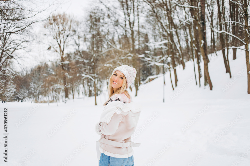 Close up portrait of an beautiful girl in a woolen sweater enjoying winter moments. Outdoors photo of a short-haired lady in a pink hat having fun on a snowy morning on a blurred nature background.