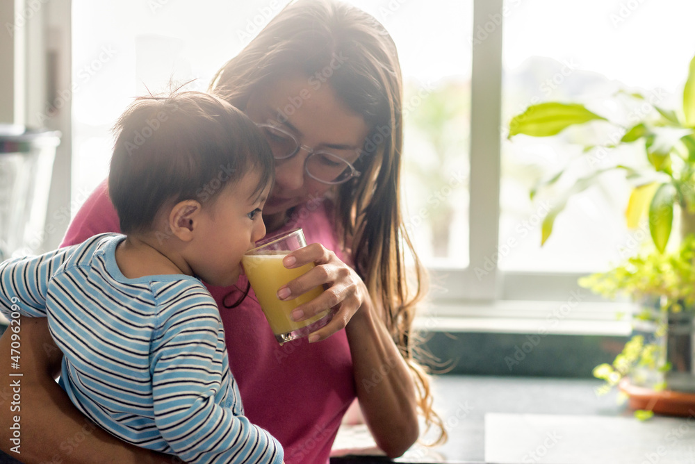 Latin baby boy zipping orange juice for breakfast near the window Latin baby boy zipping orange juice for breakfast near the window