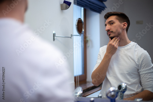 Bild auf Leinwand A guy with a patchy beard looks in the mirror