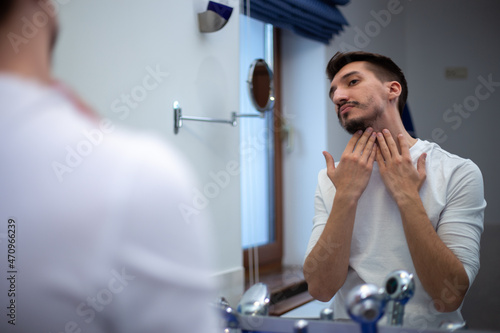 A guy with a patchy beard looks in the mirror