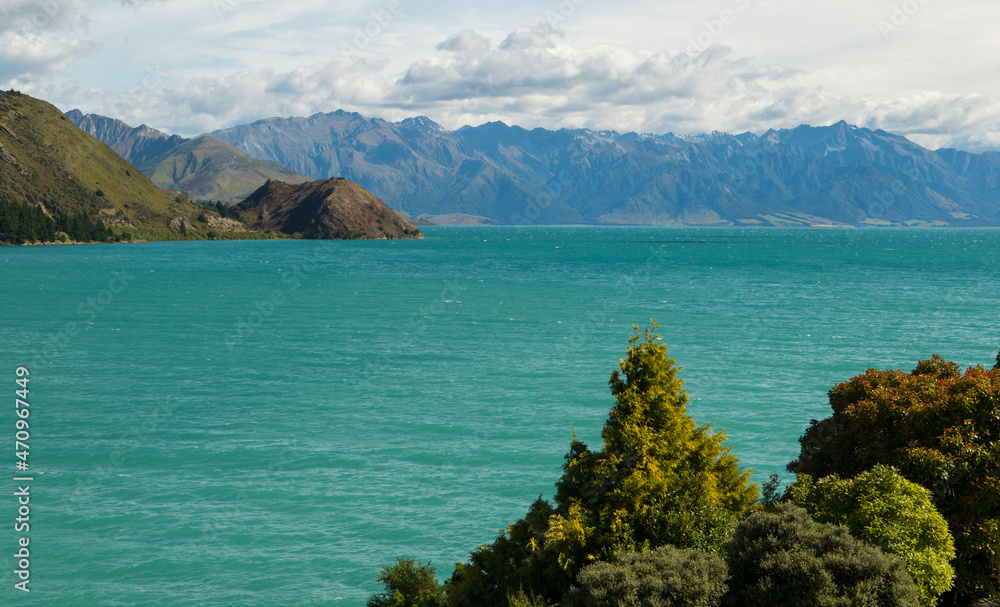 Scenic landscape view of Lake Hawea in New Zealand showing turquoise water with mountains in the background blue sky with white puffy clouds horizontal shot while on vacation holiday postcard format 